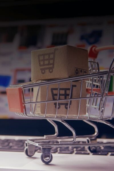 Online-Marktplätze 2026: So skalierst du profitabel mit einer Multi-Marktplatz-Strategie; auf dem Bild ist im Hintergrund und leicht verschwommen ein geöffneter Laptop zu sehen, auf dem ein Online-Shop geöffnet ist. AUf der Tastatur des Laptops ist ein Miniatur-Einkaufswagen platziert, in welchem zwei kleine Kartons gestapelt wurden. Auf den Kartons ist je ein Einkaufswagen-Icon platziert.