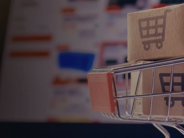 Online-Marktplätze 2026: So skalierst du profitabel mit einer Multi-Marktplatz-Strategie; auf dem Bild ist im Hintergrund und leicht verschwommen ein geöffneter Laptop zu sehen, auf dem ein Online-Shop geöffnet ist. AUf der Tastatur des Laptops ist ein Miniatur-Einkaufswagen platziert, in welchem zwei kleine Kartons gestapelt wurden. Auf den Kartons ist je ein Einkaufswagen-Icon platziert.